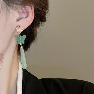 Close-up of elegant drop earrings featuring green resin butterfly and pink cat eye stone