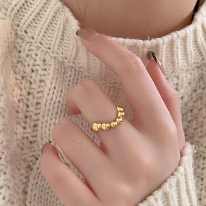 Detailed view of a gold beaded ring worn against a cozy beige knitted sweater