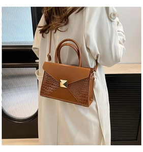 Détail d'un sac marron à texture crocodile avec boucle dorée en forme de pyramide