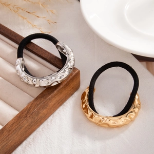Detail of gold and silver ponytail holders with hammered metal texture on wooden tray