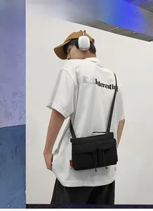 Detailed view of black nylon messenger bag with orange label on an Asian male model