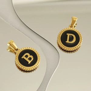 Close-up of gold 18K pendants with black enamel featuring letters B and D details