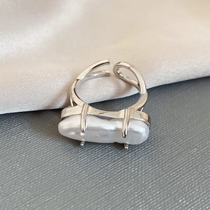Detail of baroque pearl set in silver intertwined open ring on silk background