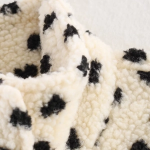 Close-up of white teddy fleece baseball jacket fabric with black heart polka dots