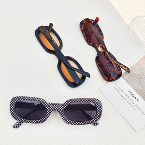 Flat lay of oval sunglasses in checkerboard, tortoise, and black frames with orange lenses