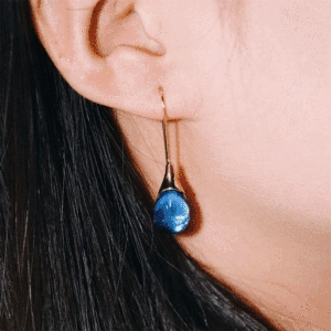Close-up of elegant blue teardrop dangle earring with golden hook on model