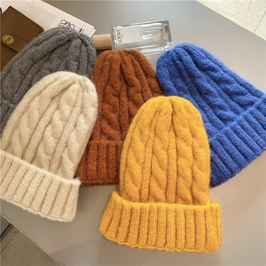 Flat lay of thick cable knit beanies in gray, beige, blue, yellow, and caramel colors