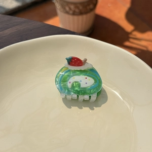 Detailed top view of a green strawberry roll cake acrylic hair claw clip on a plate