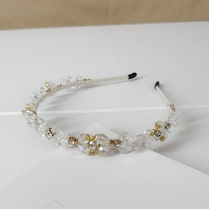 Detailed view of hand-beaded crystal headband with gold flower metal accents and white fabric