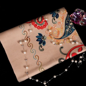 Close-up of floral embroidery on light brown cashmere scarf with pearl necklace accessory