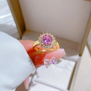 Bague marguerite en diamant rose doré portée au doigt devant une boîte à bijoux
