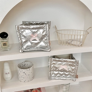 Detail of silver quilted storage bins with pink ribbon bows and white lace on a white shelf