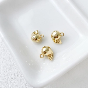 Detailed view of three 14k gold-plated 3D whale pendants in a white ceramic dish
