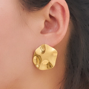 Close-up of wavy irregular gold stud earrings with a textured hammered finish for women