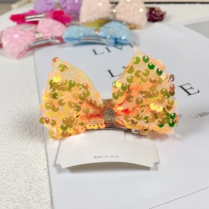 Detail of sequin mermaid bow hair clip with gold and orange sequins on a white card