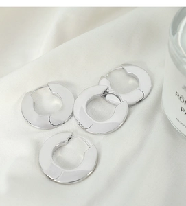 Close-up of wide polished silver hoop earrings on soft white fabric background