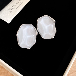 Macro shot of white oval resin earrings with silver frames on black velvet background