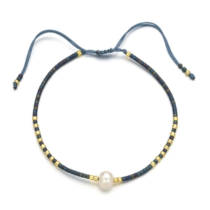 Detail of adjustable blue braided bracelet with white pearl and gold metal beads