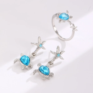Macro detail of silver starfish and turtle earrings with blue teardrop crystals