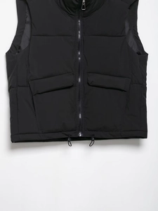 Detail of black puffer vest featuring a metal zipper, flap pockets and adjustable drawstring