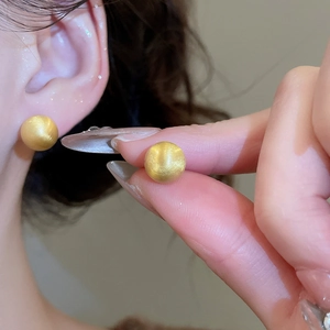 Detailed view of matte golden spherical stud earrings with elegant brushed metal texture