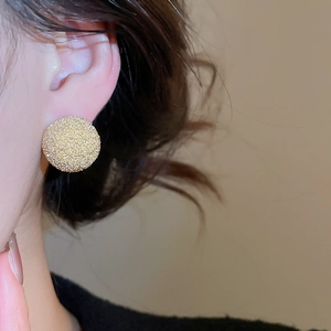 Macro view of gold round stud earrings with textured matte finish on model ear