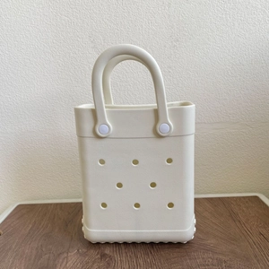 Front view of cream EVA tote bag with circular perforations on a wooden surface