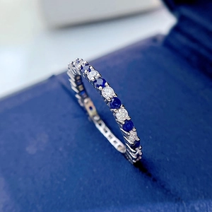 Macro shot of silver eternity ring with blue and white gems on blue velvet box