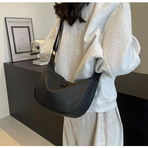 Close-up of a black crescent crossbody bag with wide strap on a model from the back