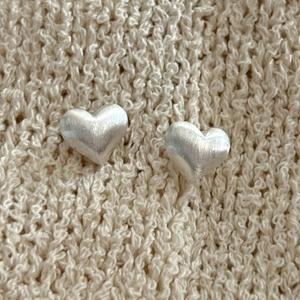 Minimalist 925 sterling silver heart earrings with a brushed matte finish on beige knit