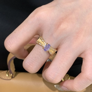 Detailed close-up of a golden bow ring with a purple gemstone and zircon accents