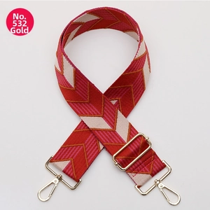 Detail of red and pink geometric woven bag strap with polished gold metal buckles