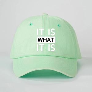 Detailed close-up of mint green baseball cap with IT IS WHAT IT IS printed slogan