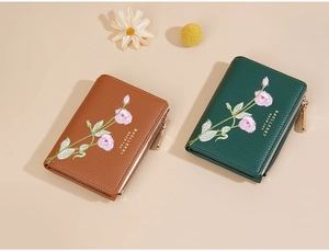 Detail of short wallets with floral embroidery and golden zippers in brown and dark green