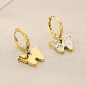 Elegant gold butterfly hoop earrings with white shell inlay on a soft beige surface