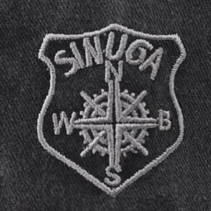 Détail du logo boussole SINUGA brodé sur le tissu gris délavé d'une casquette de baseball
