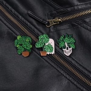Detail showing three enamel pins with monsteras and skeletons on black leather jacket