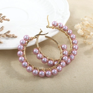 Macro detail of handmade gold hoop earrings with light purple pearl beads and wire wrap
