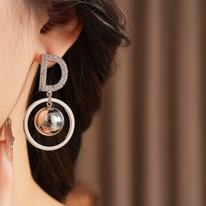 Close-up of silver letter D earring with pavé rhinestones and a spherical metal pendant