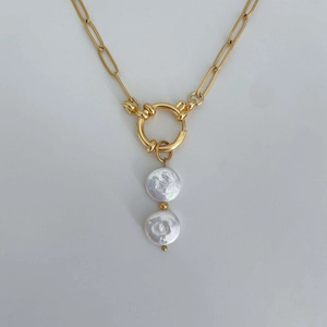 Detail of a golden chain necklace featuring a round clasp and irregular white pearls