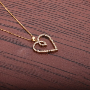 Detailed close-up of a golden heart pendant necklace with zircon inlay on wood surface