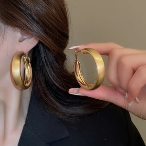 Detail of 40-50mm golden hoop earrings featuring brushed and polished metal textures