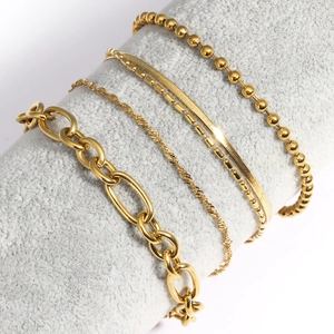 Détail d'un lot de 5 bracelets dorés superposés sur un support gris chic