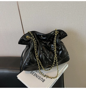 Detail of black quilted shoulder bag featuring gold chain strap on books