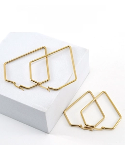 Detailed view of two pairs of gold geometric hoop earrings on a minimalist white stone pedestal