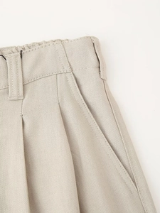 Detail of beige cotton-linen trousers showing elastic waist with pleats and side pockets
