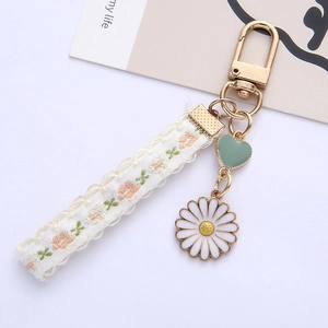 Minimalist daisy keychain with beige lace strap and green heart charm on a clean background