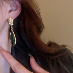 Close-up of vintage emerald glass teardrop earrings worn by a model in soft lighting