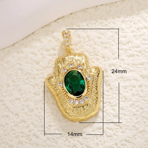 Gold Hamsa hand pendant with green gemstone and clear zircons on beige surface