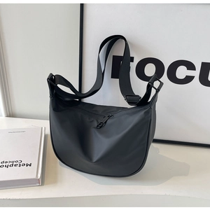 Detail of a medium black nylon crescent crossbody bag on a minimalist white table